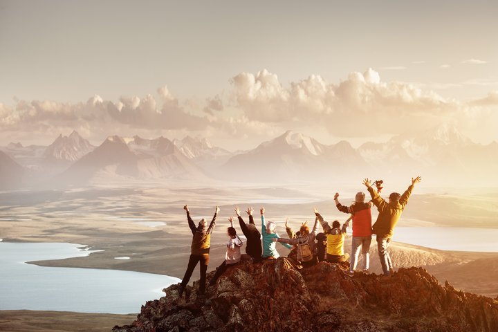 Team - Gruppe von Mitarbeiter:innen auf einem Berggipfel bei Sonnenaufgang